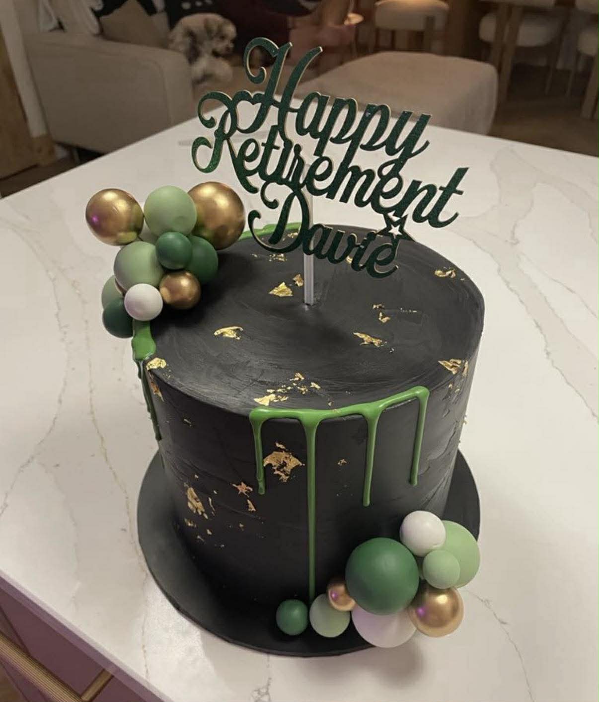 Black and gold-leaf drip cake reading 'Happy Retirement Davie', made by Flour Power Bakes